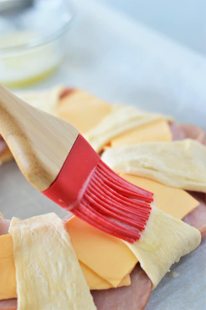 melted butter being brushed on ham and cheese crescent ring