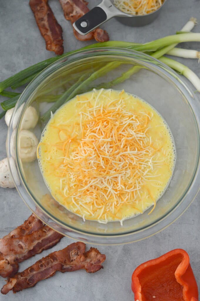 eggs, milk and shredded cheese in glass mixing bowl