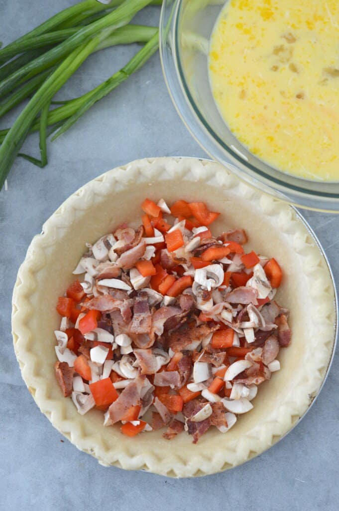 red peppers, bacon and chopped mushrooms in pie crust with quiche egg mixture in background