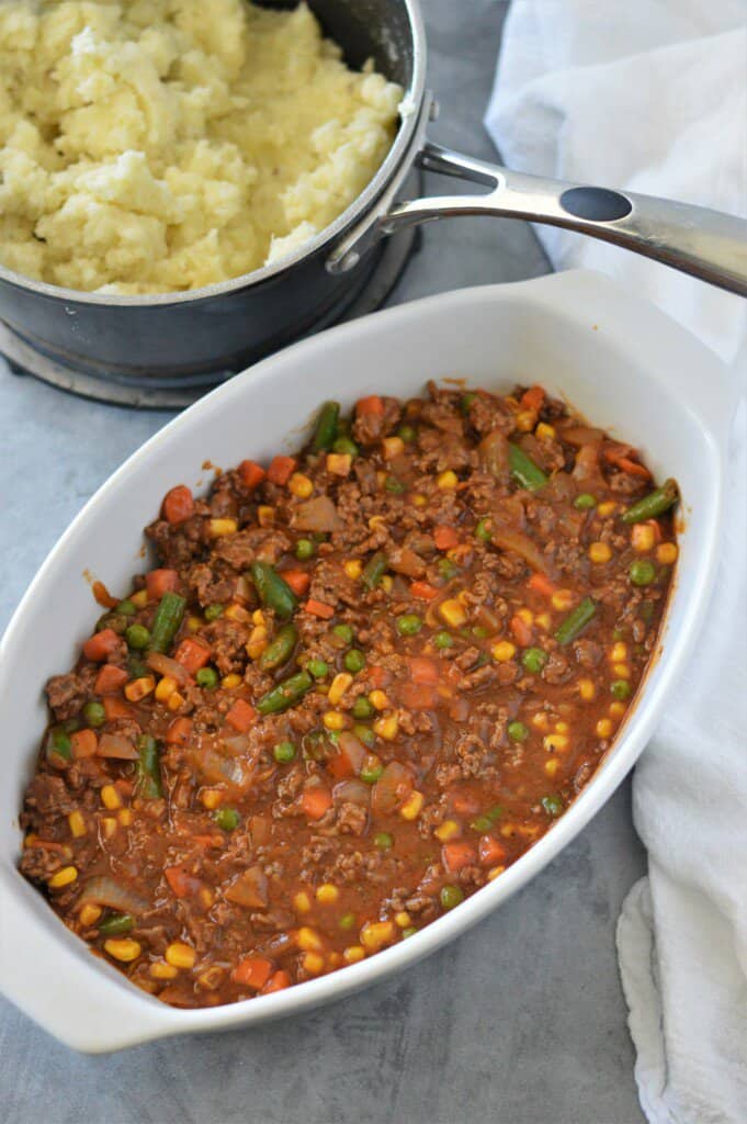 cottage pie filling in white baking dish with mashed potatoes in background