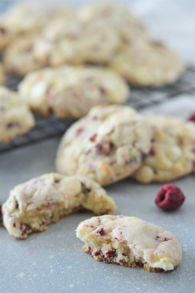 white chocolate raspberry cookie broken in half on counter with cooling rack full of cookies in background