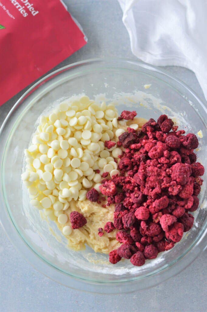 white chocolate chips and freeze dried raspberries added to cookie dough in glass bowl