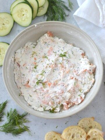 A bowl of smoked salmon dip with cucumbers and crackers.