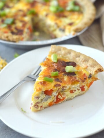 slice of quiche on white plate with fork and pan in background