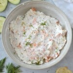 A bowl of salmon dip with cucumbers and bread.