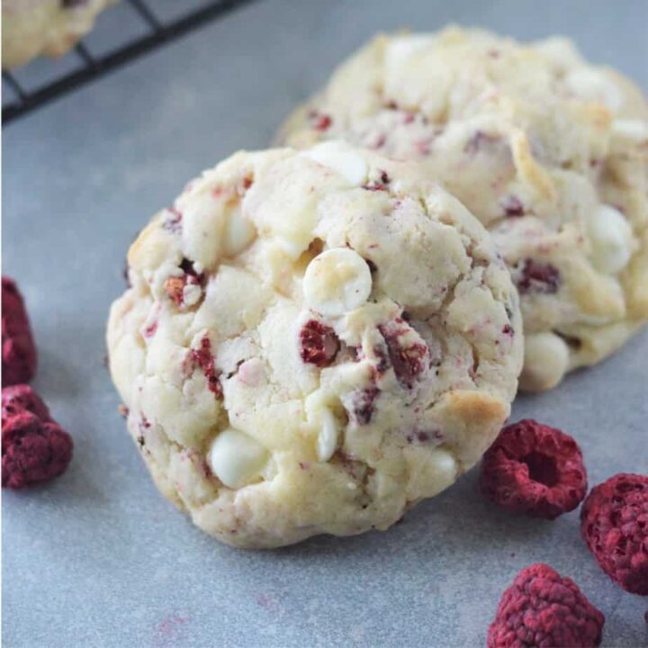 square image of two white chip raspberry cake mix cookies with freeze dried raspberries in foreground