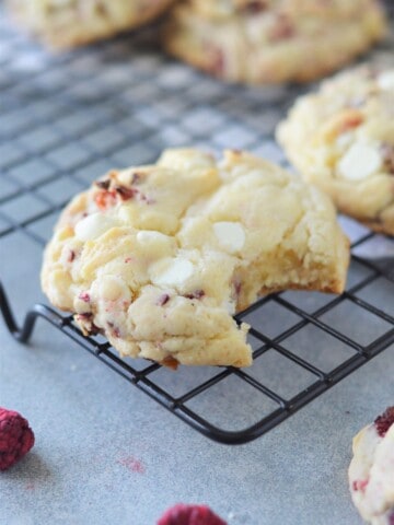white chocolate chip raspberry cake mix cookies on cooling rack one with bite taken