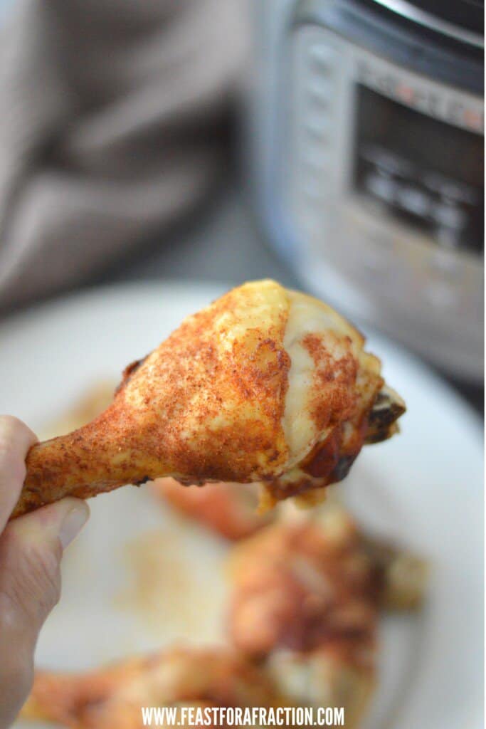 A person holding a piece of chicken in front of an instant pot.