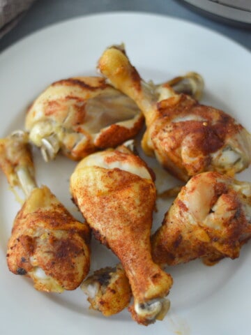 Chicken legs on a plate in front of an Instant Pot, making it easy to cook delicious chicken legs.