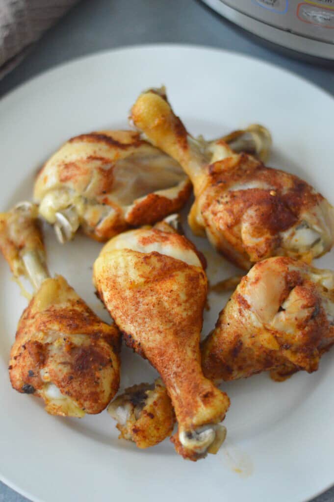 Chicken legs on a plate in front of an Instant Pot, making it easy to cook delicious chicken legs.