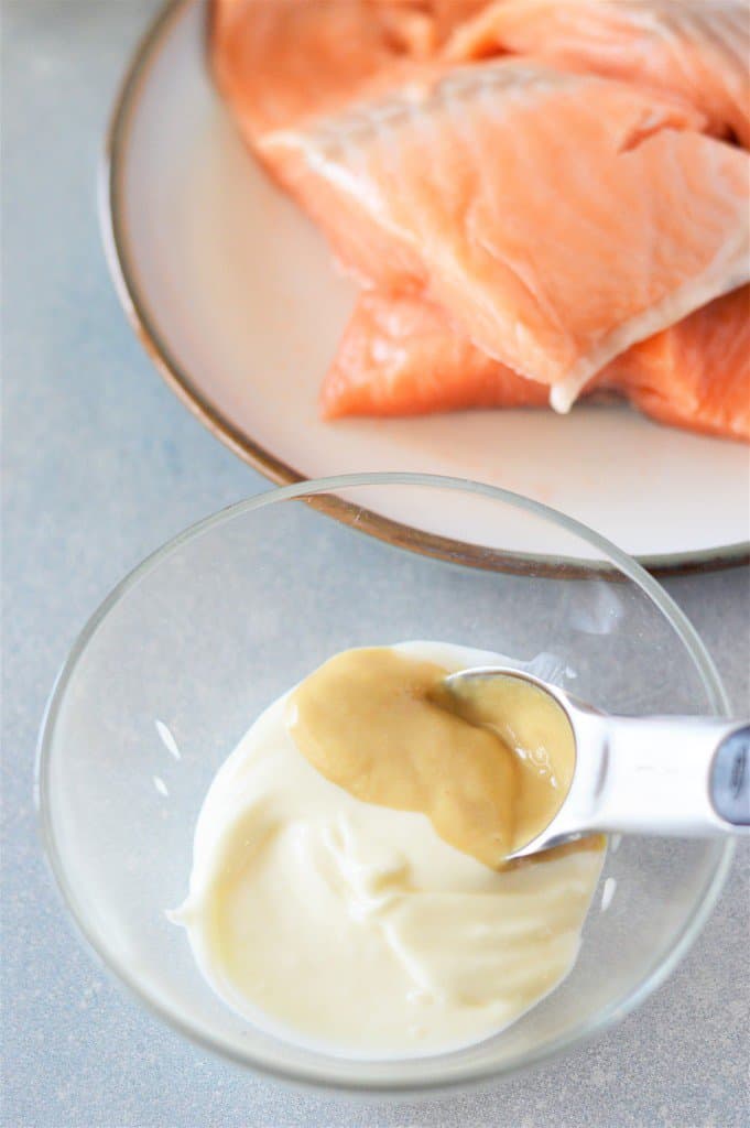 A bowl of salmon with a spoon next to a bowl of mayo and dijon mustard.