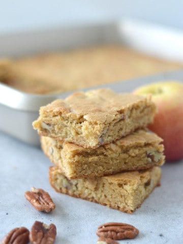 A stack of apple pecan bars with apples and pecans.
