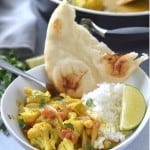 A bowl of cauliflower chickpea curry with rice and naan.