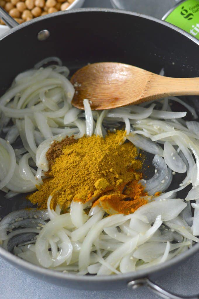 Onions and spices in a pan with a wooden spoon.