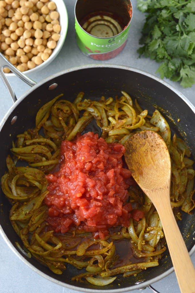onions and tomatoes in a pan with a wooden spoon with chickpeas in background