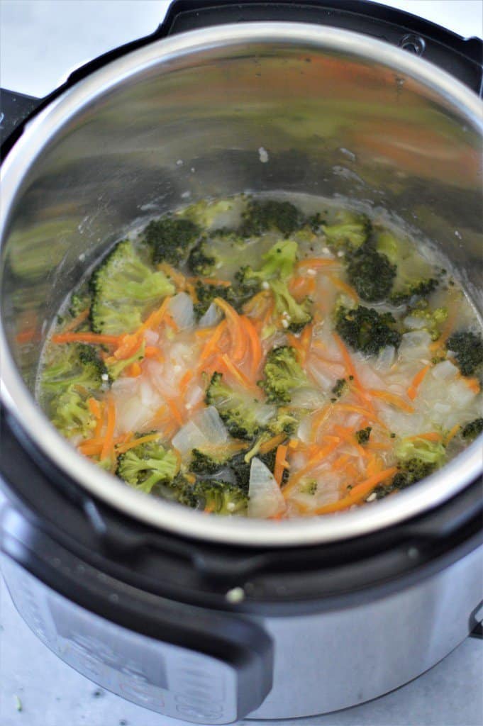 An instant pot filled with broccoli, onions, carrots, and vegetable stock.