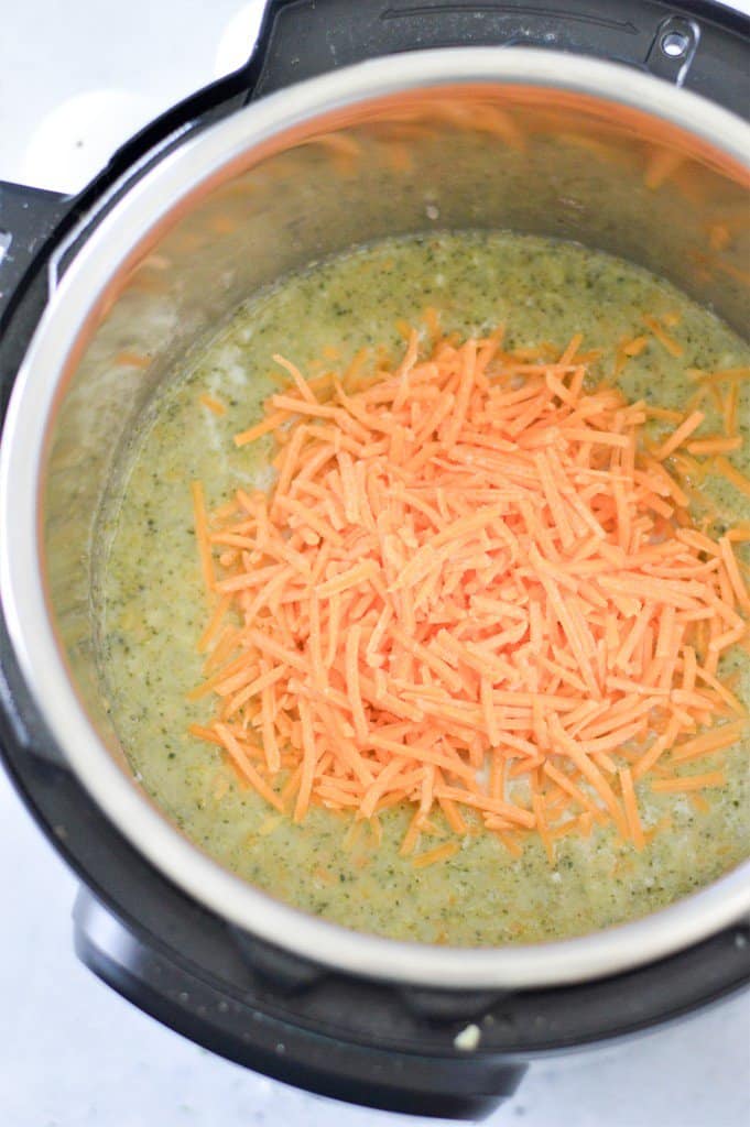 An instant pot filled with broccoli soup and shredded cheese on top