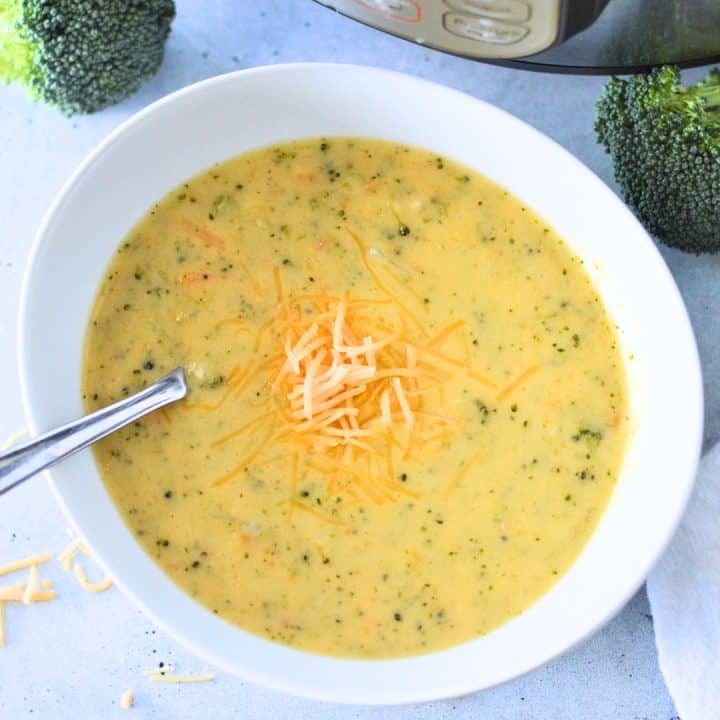 A bowl of soup with broccoli and cheese in front of an instant pot.