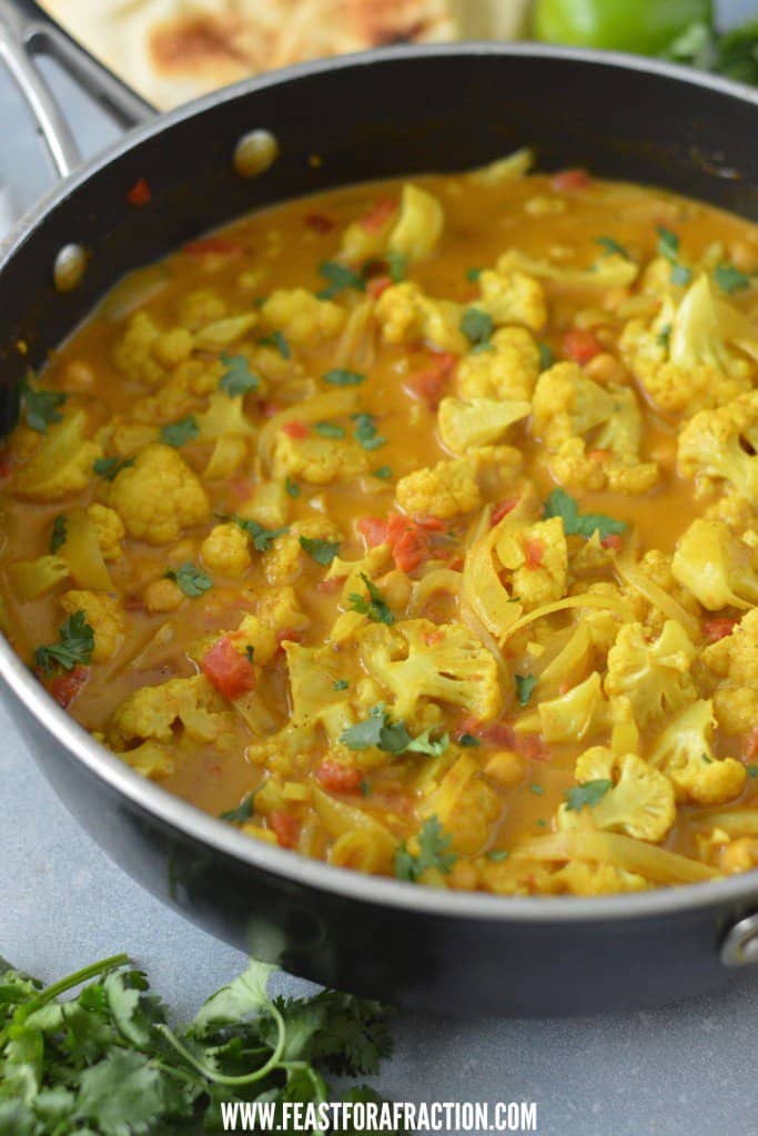 Cauliflower chickpea curry in a pan on a table garnished with cilantro