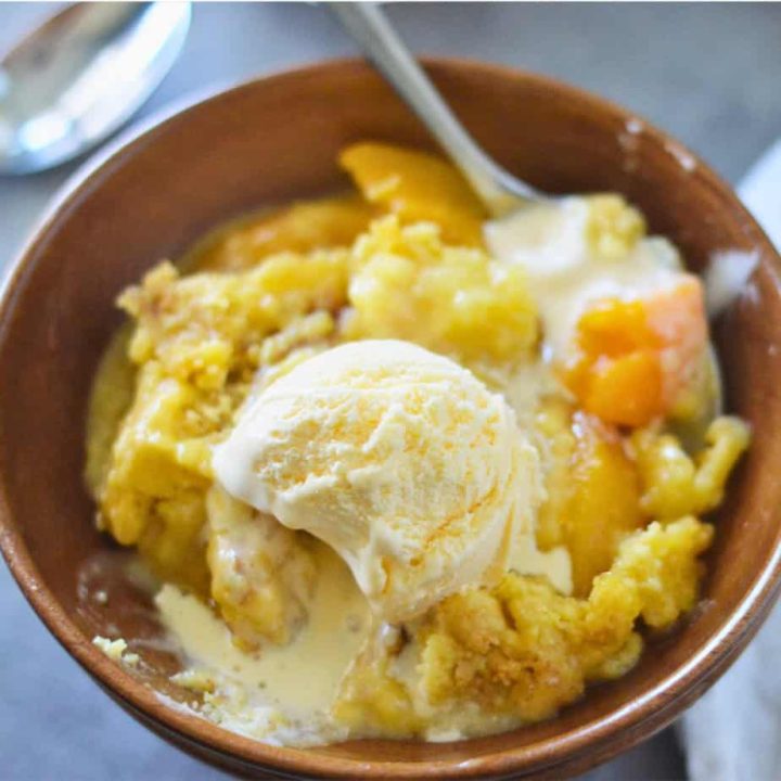Peach cobbler in a bowl with ice cream.
