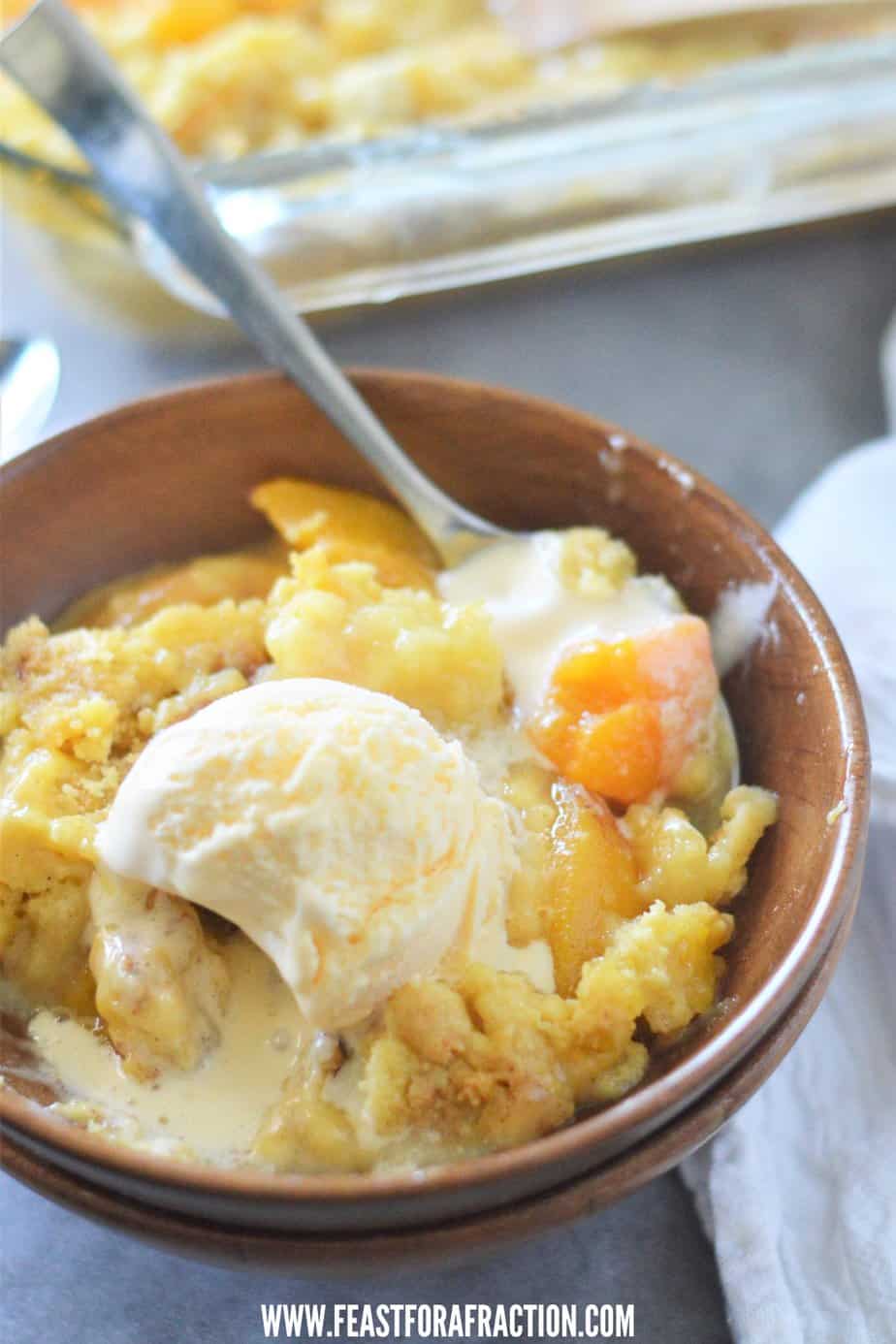 This image shows a serving of peach cobbler in a bowl topped with a scoop of vanilla ice cream. 