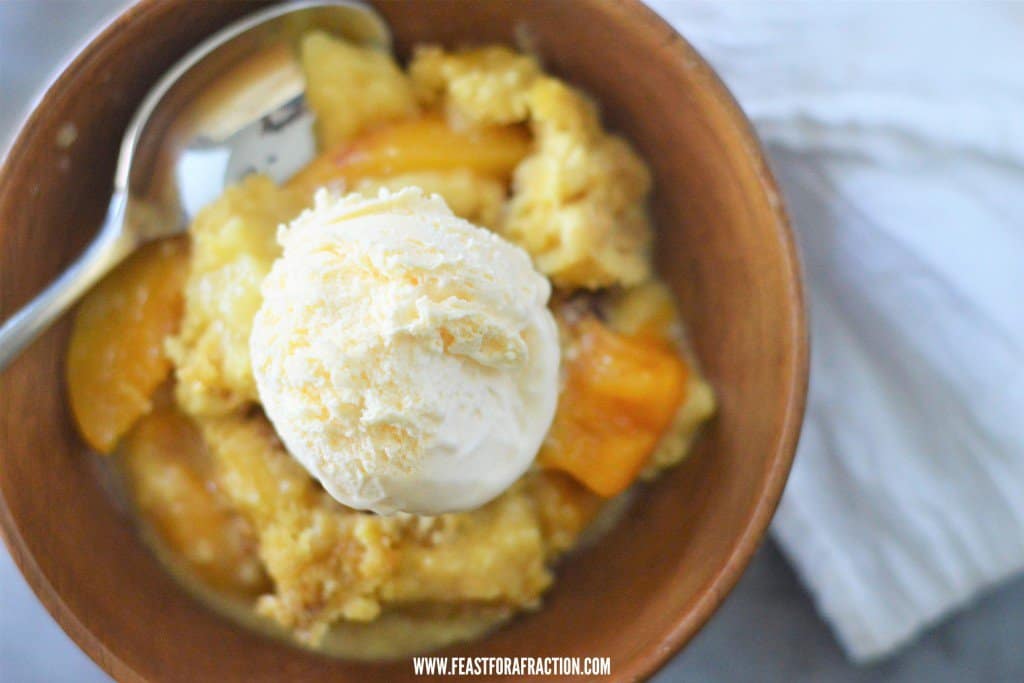 A bowl of peach cobbler dump cake with a scoop of ice cream.