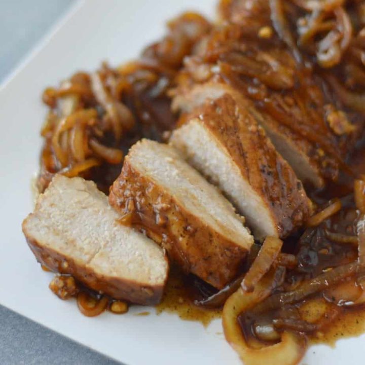 sliced pork loin with caramelized onion sauce on white plate