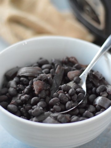 Black beans and onions in a bowl with a spoon.