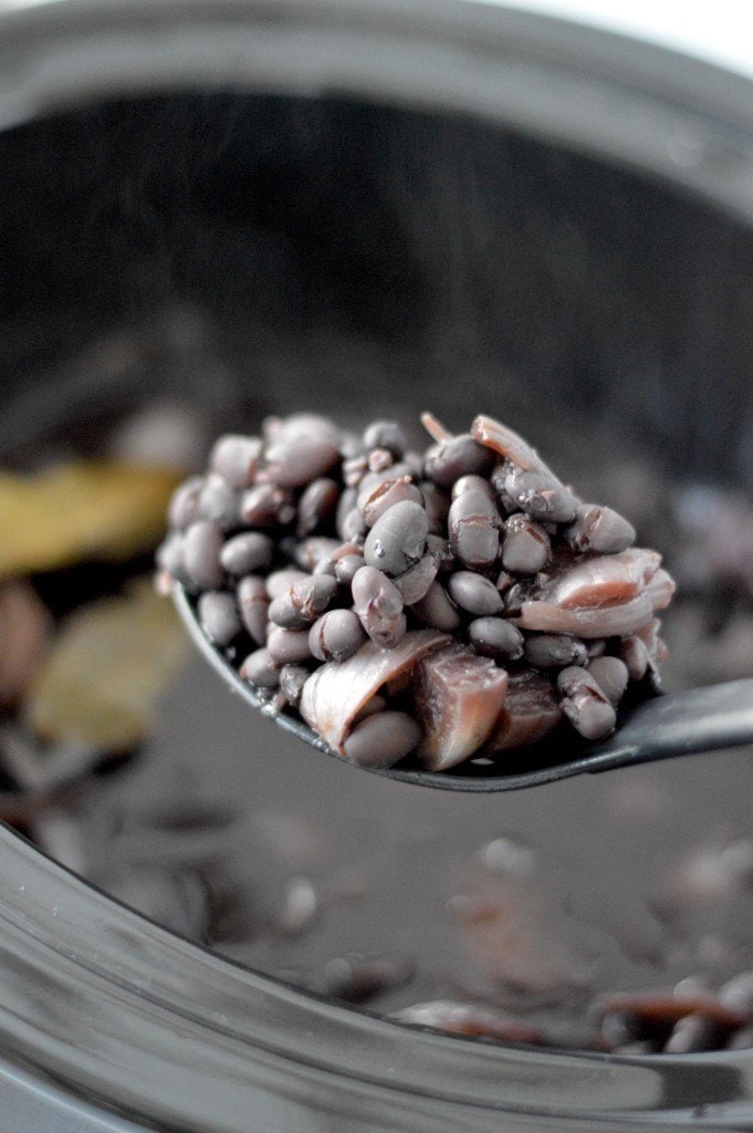A spoon full of black beans in a slow cooker.