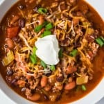 overhead view of beef irish chili in white bowl with sour cream and shredded cheese