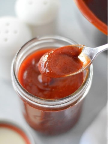 homemade no-cook bbq sauce in a mason jar with spoon. salt and pepper shakers in background