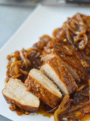 Pork loin on a white plate with onions.