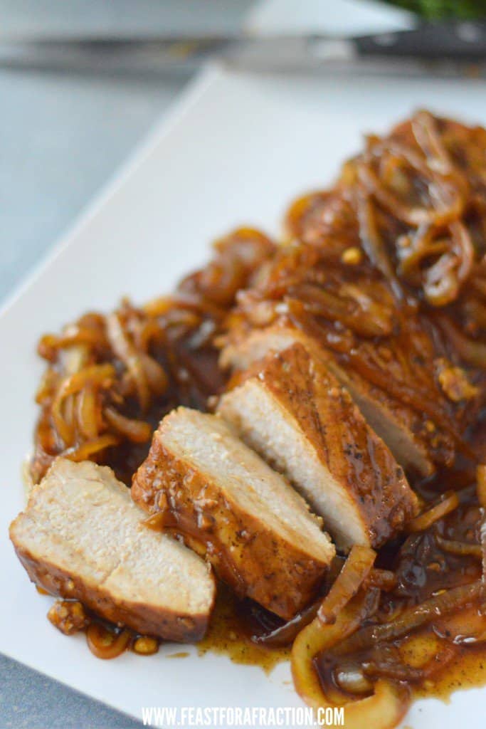 Pork tenderloin on a white plate with onions.