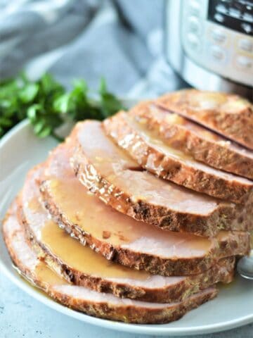 boneless ham sliced on white plate with glaze and instant pot pressure cooker in background