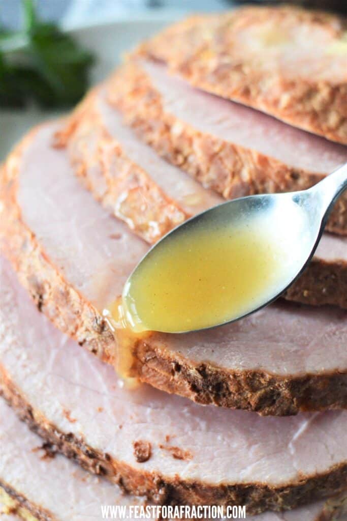 spoon pouring glaze over a sliced ham