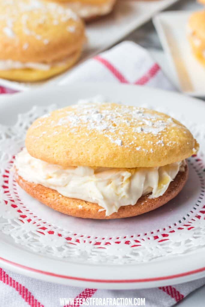 A cream cheese frosting-filled whoopie pie on a decorative white doily dusted with powdered sugar.