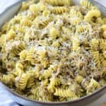 A bowl of cooked rotini pasta mixed with pesto sauce and tuna and topped with grated parmesan cheese.