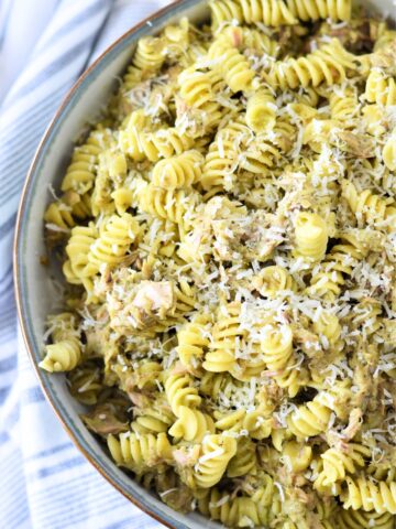 A bowl of rotini pasta mixed with tuna and pesto viewed from above.