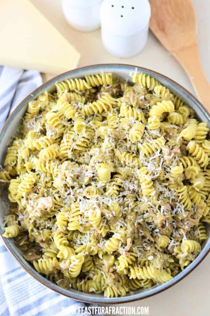 A bowl of pesto tuna pasta topped with grated cheese.
