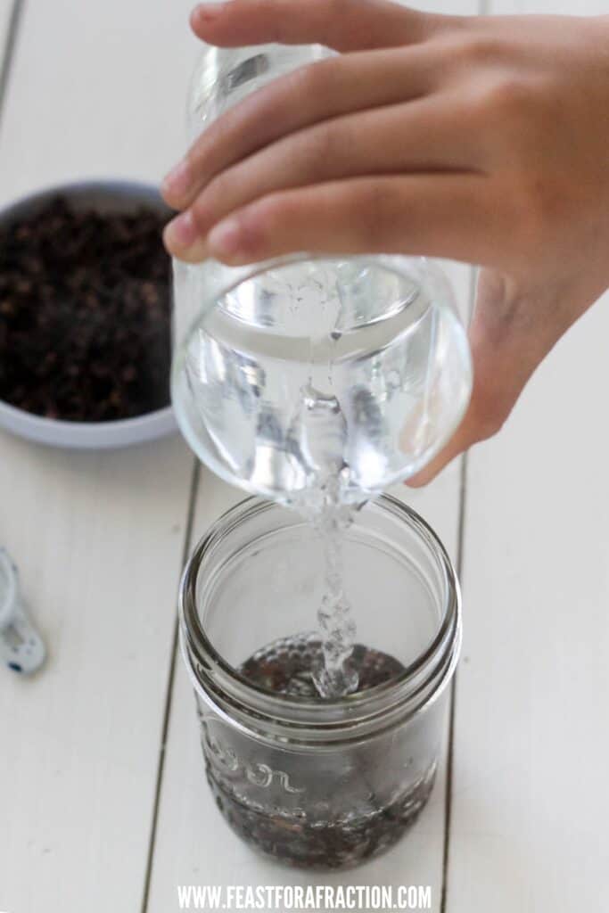 water being poured into a mason jar containing whole cloves