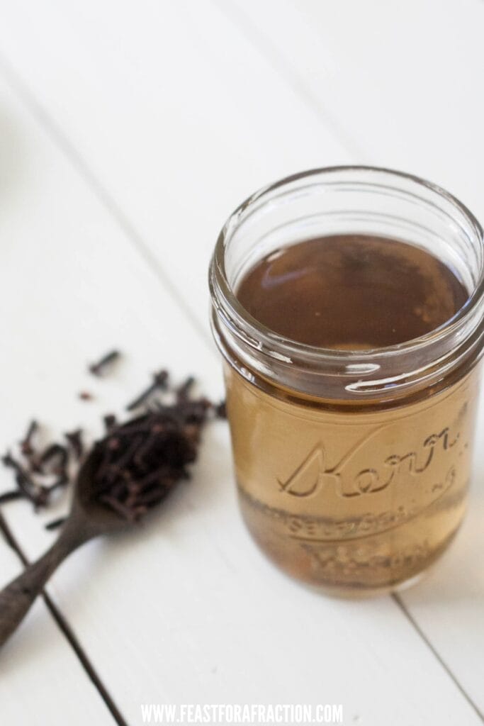 jar of homemade clove mouthwash with wooden spoon filled with whole cloves in background