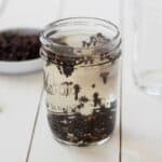 A glass jar with cloves soaking in water on a wooden surface.