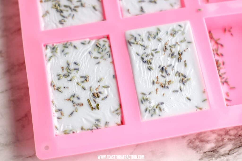 Lavender-infused white chocolate bars in a pink silicone mold, with scattered lavender buds on a marble surface.