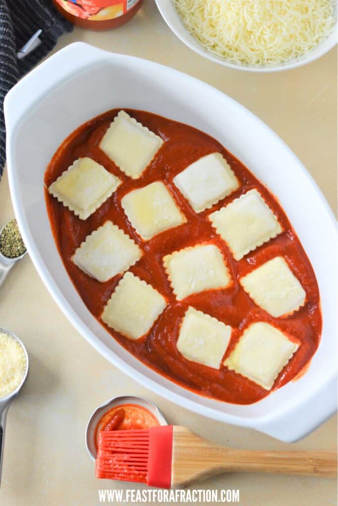 frozen ravioli layered in a baking dish with marinara sauce