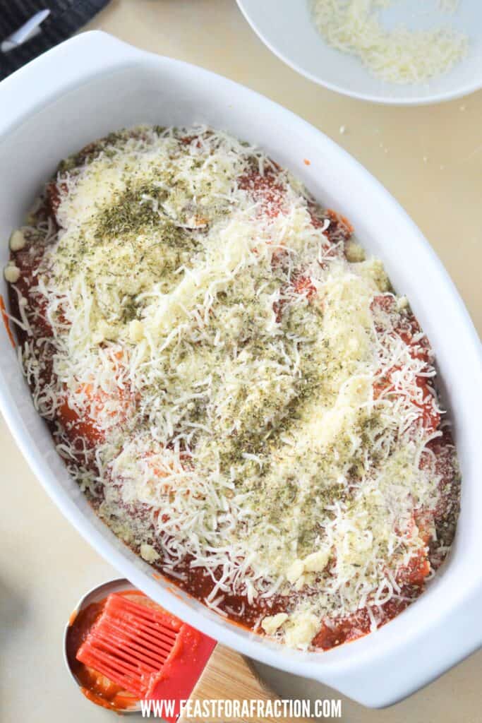 shredded mozzarella cheese on top of ravioli and pasta sauce in white baking dish