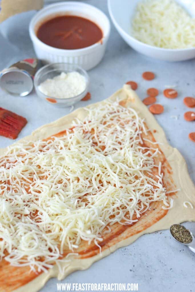 pizza sauce and mozzarella cheese spread on crescent dough pressed into rectangle; bowls of sauce and cheese in background