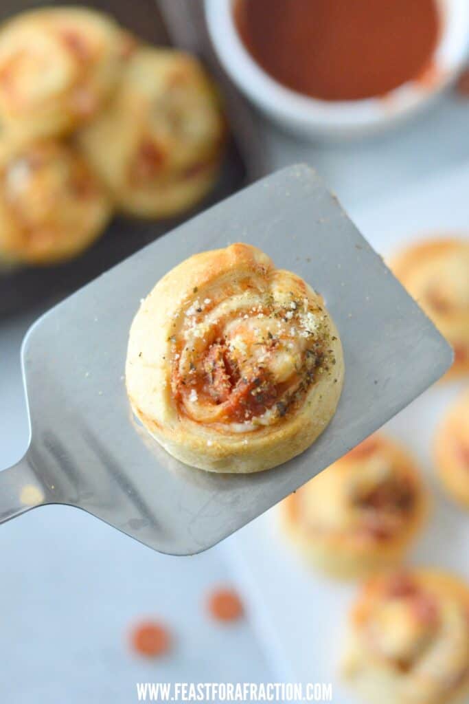 pepperoni pizza pinwheel on metal spatula with sauce and pan in background