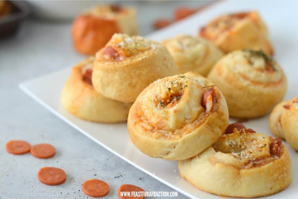 horizontal image of baked pizza pinwheels on white square plate with mini pepperonis on counter
