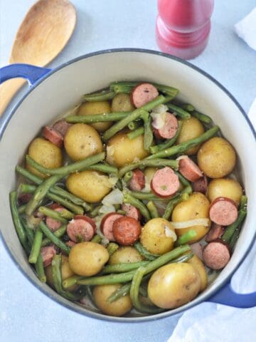 overhead view of hoosier stew in dutch oven with wooden spoon and pepper grinder on counter